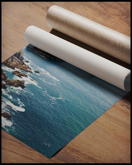 Ein Poster vom Blick auf das blaue Meer und mehrere Felsformationen die aus dem Wasser blicken, gerollt auf einer Holzoberfläche liegend