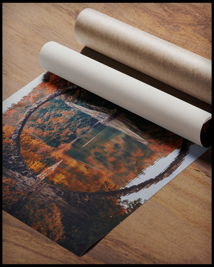 Ein Poster von der Seitenansicht einer freispannenden Bogenbrücke in einem herbstlichen Wald und über einem ruhigen See, gerollt auf einer Holzoberfläche liegend