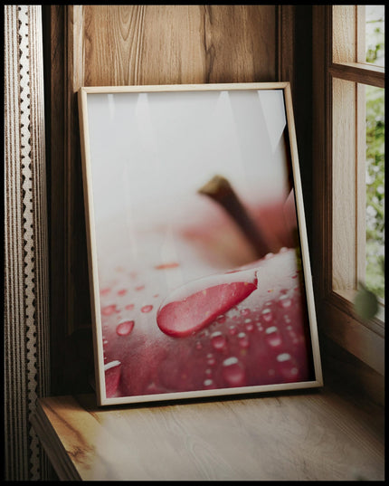 Ein gerahmtes Poster von einem roten Apfel mit Wassertropfen in Nahaufnahme, vor einem Fenster an die Wand angelehnt