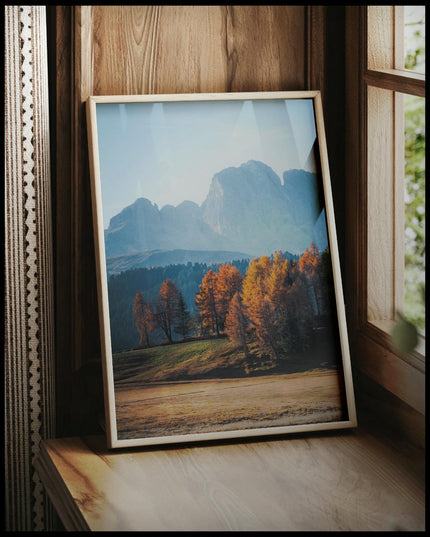 Ein gerahmtes Poster von herbstlich gefärbten Bäumen vor einer Berglandschaft in den Dolomiten, vor einem Fenster an die Wand angelehnt