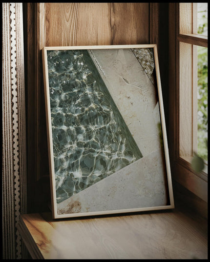 Ein gerahmtes Poster von einem Swimming Pool aus Marmor mit einem Mosaikmuster auf dem Beckengrund, vor einem Fenster an die Wand angelehnt